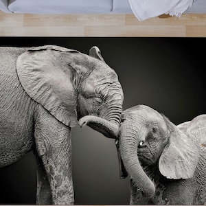 May include: A black and white photograph of two elephants, one large and one small, standing close together. The larger elephant is touching the smaller elephant with its trunk.