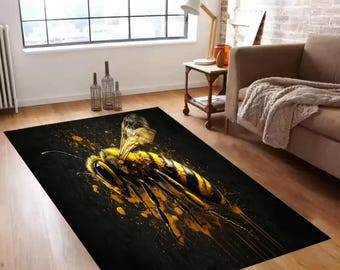 May include: A rectangular black rug featuring a large, detailed illustration of a bee. The bee is depicted in yellow and black, with a splash of yellow paint-like accents. The rug is placed on a wooden floor in a living room setting.