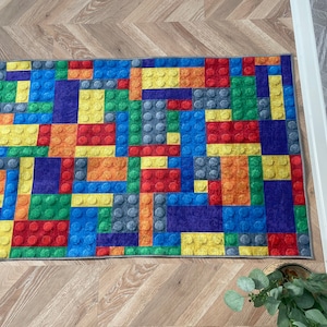May include: A colorful rug with a design that resembles a pattern of colorful toy building blocks. The rug is made of a soft, plush material and is perfect for adding a playful touch to any room.