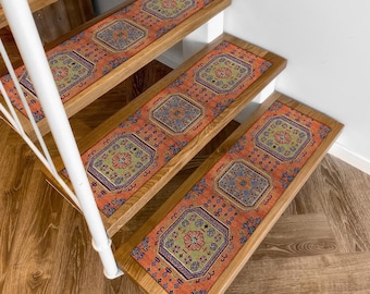 Puede incluir: Peldaños de escalera con un diseño de alfombra tradicional. Las huellas presentan un fondo naranja con un patrón repetitivo de formas florales y geométricas en azul, verde y crema. Las escaleras de madera tienen una barandilla blanca.