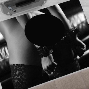 Puede incluir: Fotografía en blanco y negro de una persona que lleva una liga de encaje negro y un arnés de cuero con correas. La cara de la persona está oscurecida por un círculo negro.