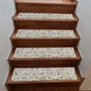 Könnte beinhalten: Treppenstufen mit cremefarbenem Hintergrund und einem sich wiederholenden Blumenmuster in Grau- und Blautönen. Die rechteckigen Stufen sind auf Holztreppen platziert. Die Treppe hat einen warmen, braunen Farbton.