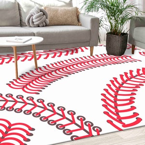 May include: White area rug with a baseball design. The rug features a repeating pattern of red baseball stitching on a white background. The rug is in a living room setting with a sofa, coffee table, and plant.