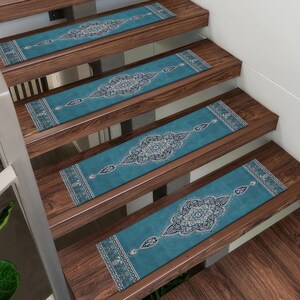 May include: Stair treads with a teal and ivory ornate design are installed on wooden stairs. The treads feature a central medallion pattern with a border design. The stairs have a dark wood finish.