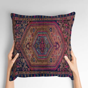 May include: Square pillow with a vintage rug design. The pillow features a central geometric pattern in shades of brown, blue, and pink, with intricate border details. The overall aesthetic is reminiscent of traditional oriental rugs.