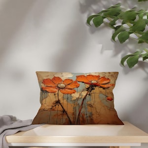 May include: Rectangular cushion with an abstract floral design. The artwork depicts two large orange flowers with white centres against a backdrop of muted blues and browns. The painting has a textured, impasto style. The cushion is on a light-coloured wooden surface.