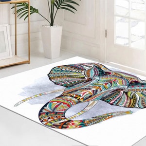 May include: A white area rug with a colorful, patterned elephant head design. The elephant's head is filled with intricate details in shades of blue, green, yellow, red, and orange.