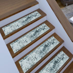 May include: Stair treads with a distressed abstract pattern in shades of blue, gray, and white. The treads are rectangular and placed on wooden stairs with a light brown finish. The design adds a modern touch to the staircase.