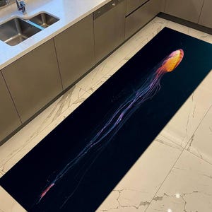 K&ouml;nnte beinhalten: Ein langer, rechteckiger K&uuml;chenteppich mit einem Quallen-Design. Die Qualle hat eine gelb-orangefarbene Glocke mit langen, flie&szlig;enden Tentakeln in Lila und Blau vor einem dunkelblauen Hintergrund. Der Teppich liegt auf einem wei&szlig;en Fliesenboden.