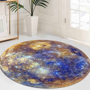 May include: A round rug with a blue and gold design that resembles the surface of a planet. The rug is on a white floor in a room with a window and a shelf.