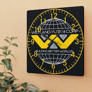 May include: Square black wall clock with a yellow and white graphic design. The clock face features the text "WEYLAND-YUTANI CORP" and "BUILDING BETTER WORLDS". The clock hands are black.