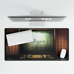 May include: A vintage-style TV screen with a test pattern that reads "PLEASE STAND BY" on a brown and gold patterned desk mat. A white keyboard and a white mouse are also on the mat.