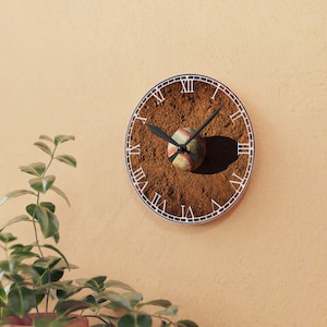 May include: A round clock with Roman numeral markings on a brown background that resembles a baseball field. A baseball is in the center of the clock face.