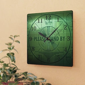 May include: Square wall clock with a green background featuring a test pattern design and the text "PLEASE STAND BY." The clock has black hands and numbers, with the time displayed. The clock is mounted on a beige wall.