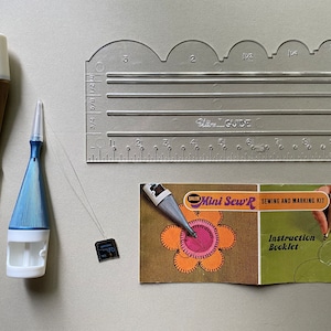 May include: A sewing and marking kit with a clear plastic ruler, a blue and white marking tool, a gold marking tool, a small black tool, and a booklet with the text "Salem Gelegt Distributor Inc. Made in USA" and "Mini Sew'R Sewing and Marking Kit Instruction Booklet".