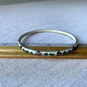 May include: A white enamel bangle bracelet with a floral design. The flowers are green, white, and pink.