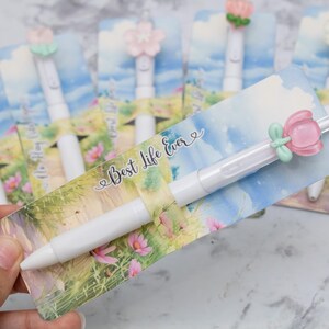 May include: White pens with flower-shaped toppers and decorative cards. The cards feature a watercolor design with the text "Best Life Ever". The pens have a smooth, white barrel and are ideal for gifts or stationery.