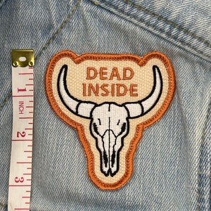 May include: Embroidered patch with a bull skull design and the words "DEAD INSIDE" in brown. The patch is approximately 3 inches tall and has a tan background with a brown border. The patch is on a light blue denim jacket.