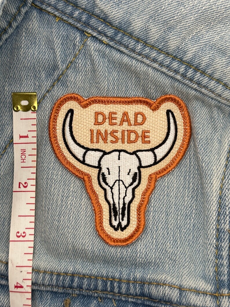 May include: Embroidered patch with a bull skull design and the words "DEAD INSIDE" in brown. The patch is approximately 3 inches tall and has a tan background with a brown border. The patch is on a light blue denim jacket.