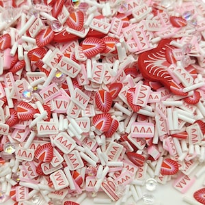 May include: A mix of red and pink polymer clay sprinkles, including strawberry slices, small squares with a pink and white pattern, and white sticks.