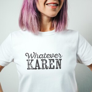 Pode incluir: Uma t-shirt branca de manga curta com o texto Whatever KAREN impresso numa fonte cinzenta escura, texturizada e com aspeto desgastado no peito. A t-shirt tem um decote redondo e um corte padrão, proporcionando um visual simples.