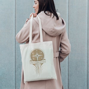 May include: A white canvas tote bag with a gold compass design and the text "WORLDHOPPER".