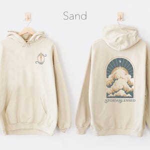 May include: Sand colored hoodie with a graphic of a cloud with the text "Stormblessed" on the back and a small graphic on the front.