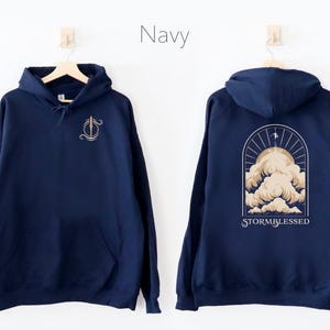 May include: Navy blue hooded sweatshirt with a graphic of a stylized cloud formation and the text "STORMBLESSED" on the back. The front of the sweatshirt has a small graphic of a sword.