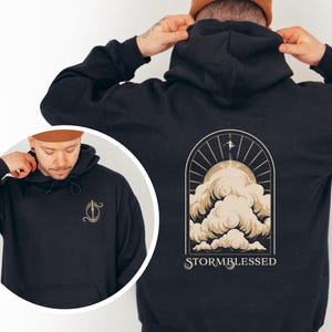 May include: Black hoodie with a graphic of a person flying above clouds with the text "STORMBLESSED" on the back. The front of the hoodie has a small graphic of a stylized letter "S" with a cloud and a lightning bolt.