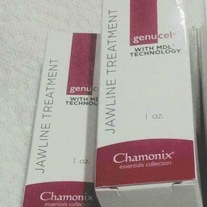 May include: Two white boxes with red accents containing a 1 ounce bottle of genucel jawline treatment. The boxes have the text "Chamonix essentials collection" on the bottom.