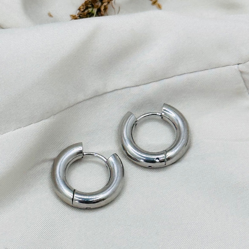 K&ouml;nnte beinhalten: Ein Paar silberne Creolen. Die Ohrringe sind schlicht und elegant, mit einer glatten, polierten Oberfl&auml;che.