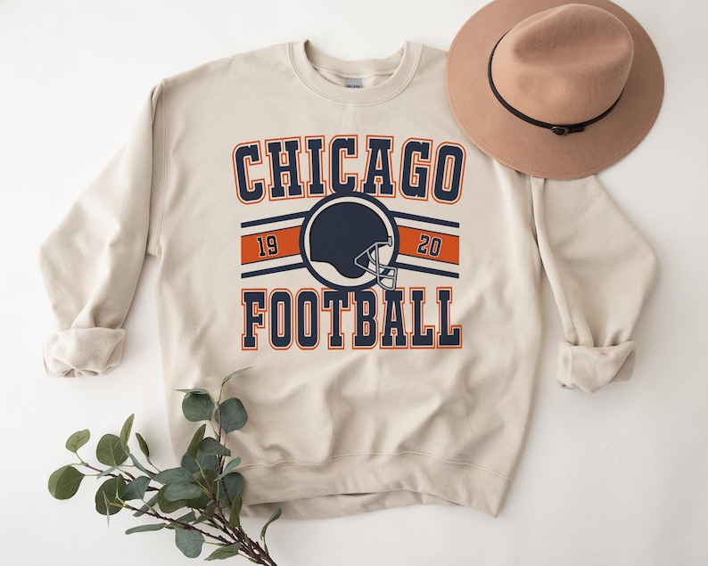May include: A beige sweatshirt with a navy blue and orange graphic that says "CHICAGO FOOTBALL" with a football helmet graphic and the numbers 19 and 20.