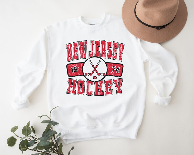 May include: White sweatshirt with a red and black graphic that says "New Jersey Hockey" with crossed hockey sticks and the numbers 19 and 74.