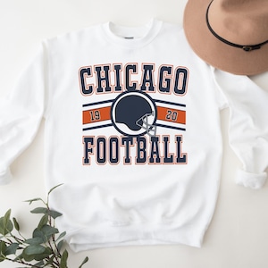 May include: White sweatshirt with a navy blue and orange graphic that says "CHICAGO FOOTBALL" with a football helmet in the center. The numbers "19" and "20" are on either side of the helmet.