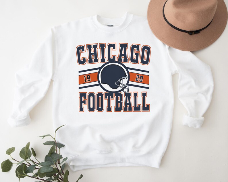 May include: White sweatshirt with a navy blue and orange graphic that says "CHICAGO FOOTBALL" with a football helmet in the center. The numbers "19" and "20" are on either side of the helmet.