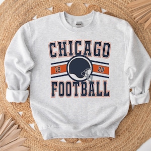 May include: Gray sweatshirt with a navy blue and orange graphic that says "CHICAGO FOOTBALL" with a football helmet in the center and the numbers "19" and "20" on either side of the helmet.