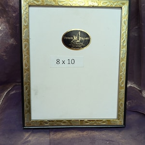 Könnte beinhalten: Schwarzer Bilderrahmen mit einem goldenen und silbernen verzierten Rahmen. Der Rahmen ist 8x10 Zoll groß und hat einen weißen Passepartout. Ein Aufkleber mit dem Text "Design In Frames" befindet sich auf dem Passepartout.