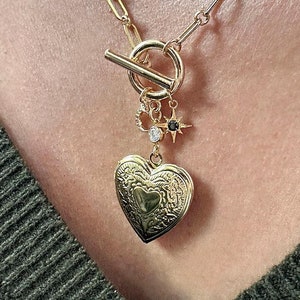 May include: A gold chain necklace with a heart-shaped locket, a star charm, and a toggle clasp.