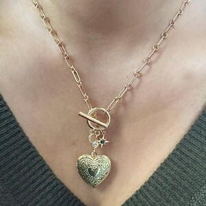 May include: A gold chain necklace with a heart-shaped locket, a toggle clasp, and small star and circle charms.