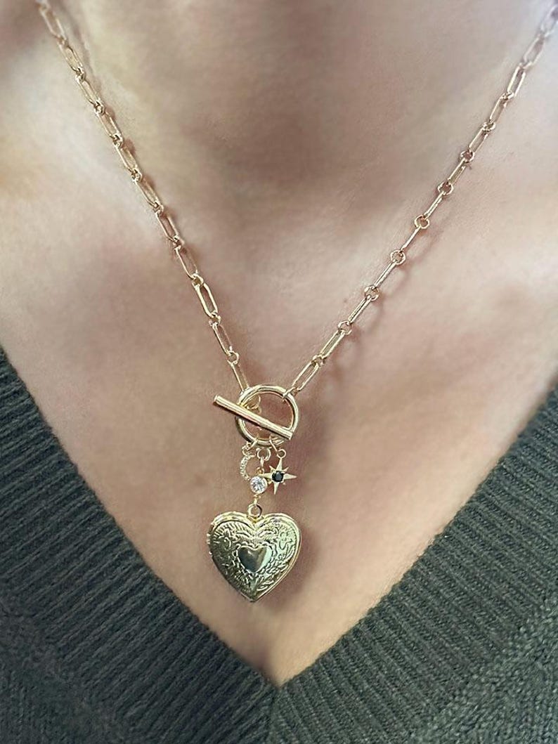 May include: A gold chain necklace with a heart-shaped locket, a toggle clasp, and small star and circle charms.