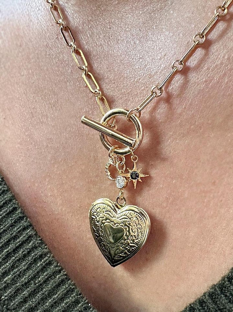 May include: A gold chain necklace with a heart-shaped locket, a star charm, and a toggle clasp.