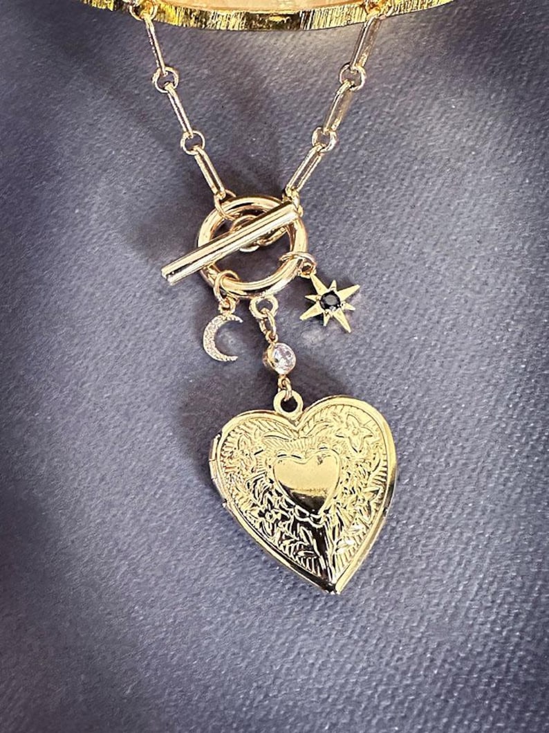 May include: A gold necklace with a heart-shaped locket, a crescent moon charm, and a star charm with a black stone. The necklace has a toggle clasp.