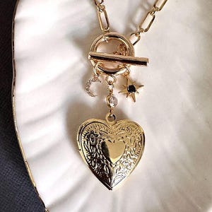 May include: A gold necklace with a heart-shaped locket, a crescent moon charm, and a star charm. The necklace has a toggle clasp.