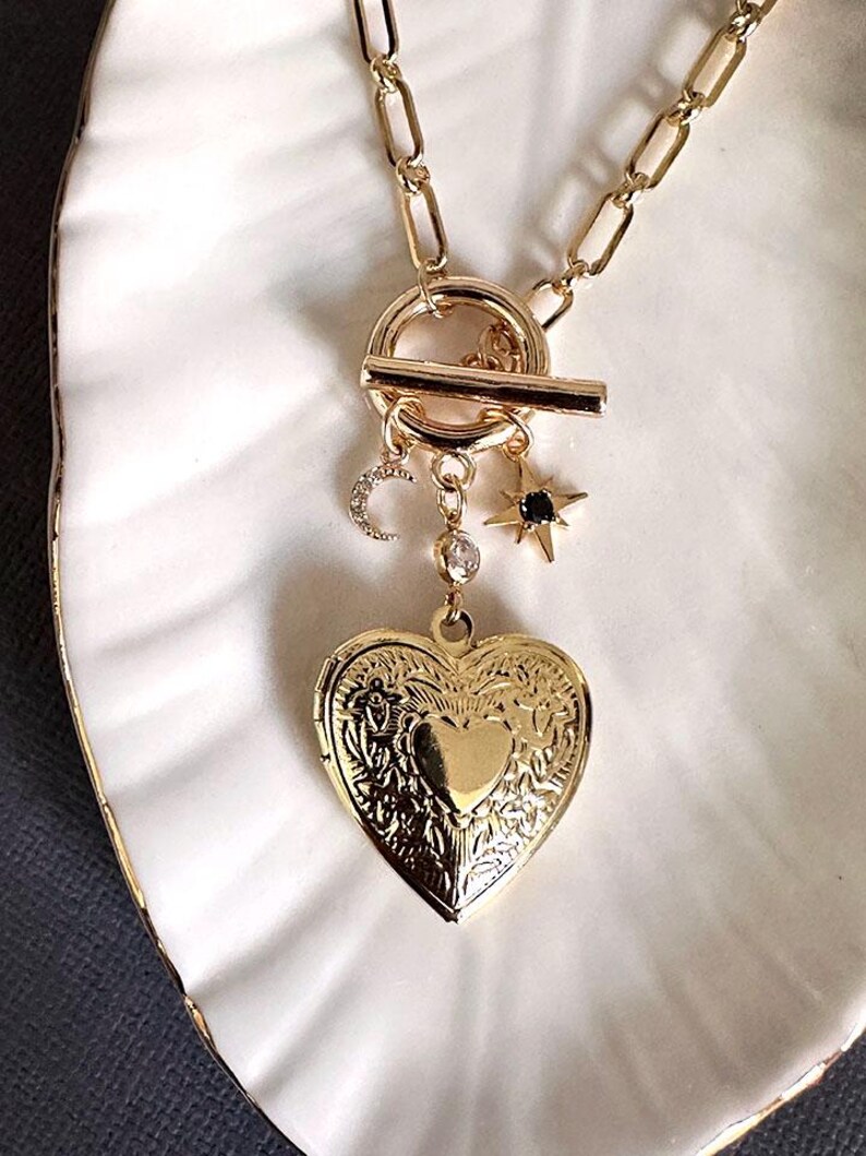 May include: A gold necklace with a heart-shaped locket, a crescent moon charm, and a star charm. The necklace has a toggle clasp.