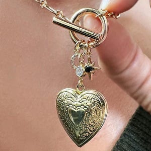 May include: A gold necklace with a heart-shaped locket, a star charm, and a crescent moon charm. The necklace has a toggle clasp.