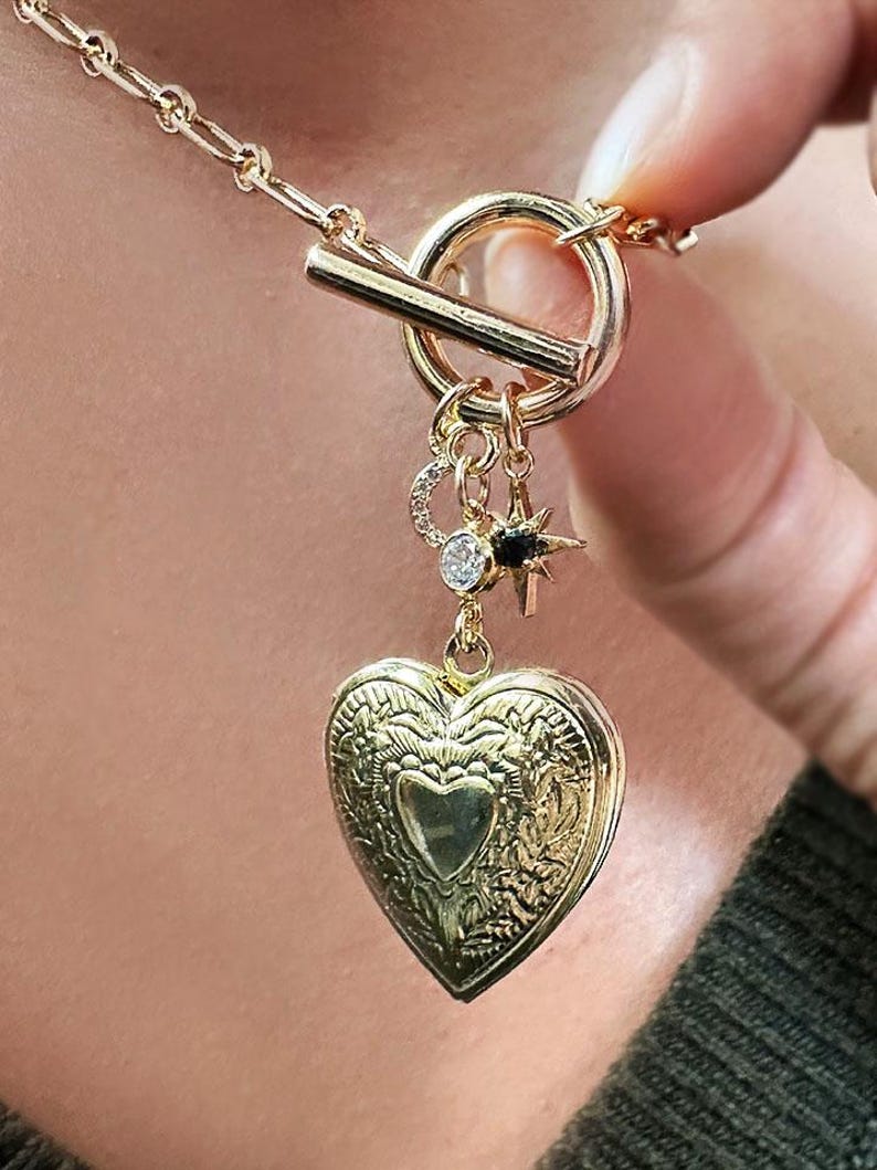 May include: A gold necklace with a heart-shaped locket, a star charm, and a crescent moon charm. The necklace has a toggle clasp.