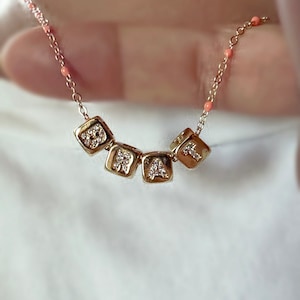 Op de afbeelding: Een gouden ketting met een delicate ketting en vijf kleine, vierkante hangers. Elke hanger is versierd met glinsterende zirkonia-stenen en heeft een letter, die het woord "LOVE" spellen.