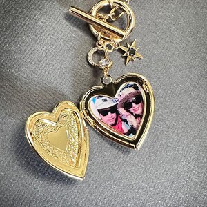 May include: Gold heart-shaped locket necklace with a photo of two people inside. The necklace has a toggle clasp and a star charm with a black stone.