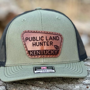 May include: A green and black trucker hat with a brown leather patch that says "Public Land Hunter Kentucky".