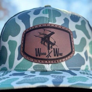 May include: A camouflage trucker hat with a brown leather patch that says "Wood x Wire".
